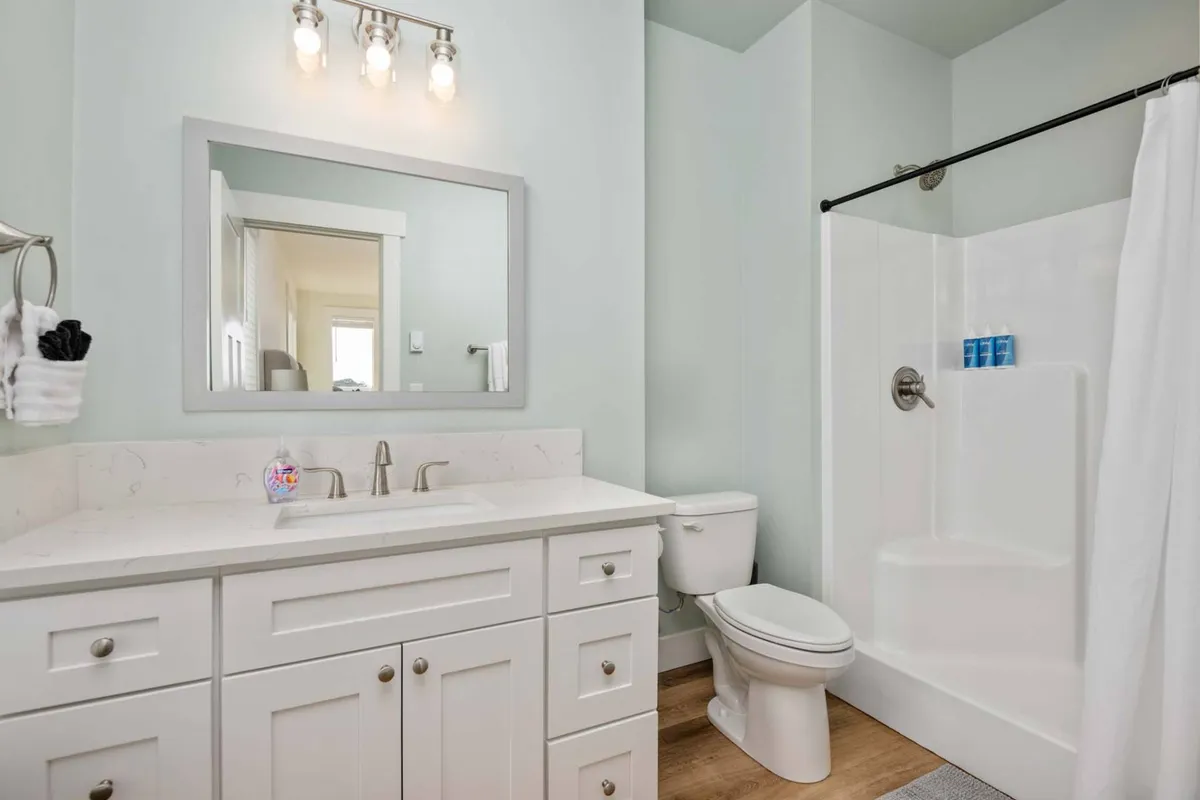 A modern en suite bathroom with a large mirror, sink, and glass-enclosed shower. The space is bright, clean, and well-appointed, offering a spa-like atmosphere for personal care and relaxation.