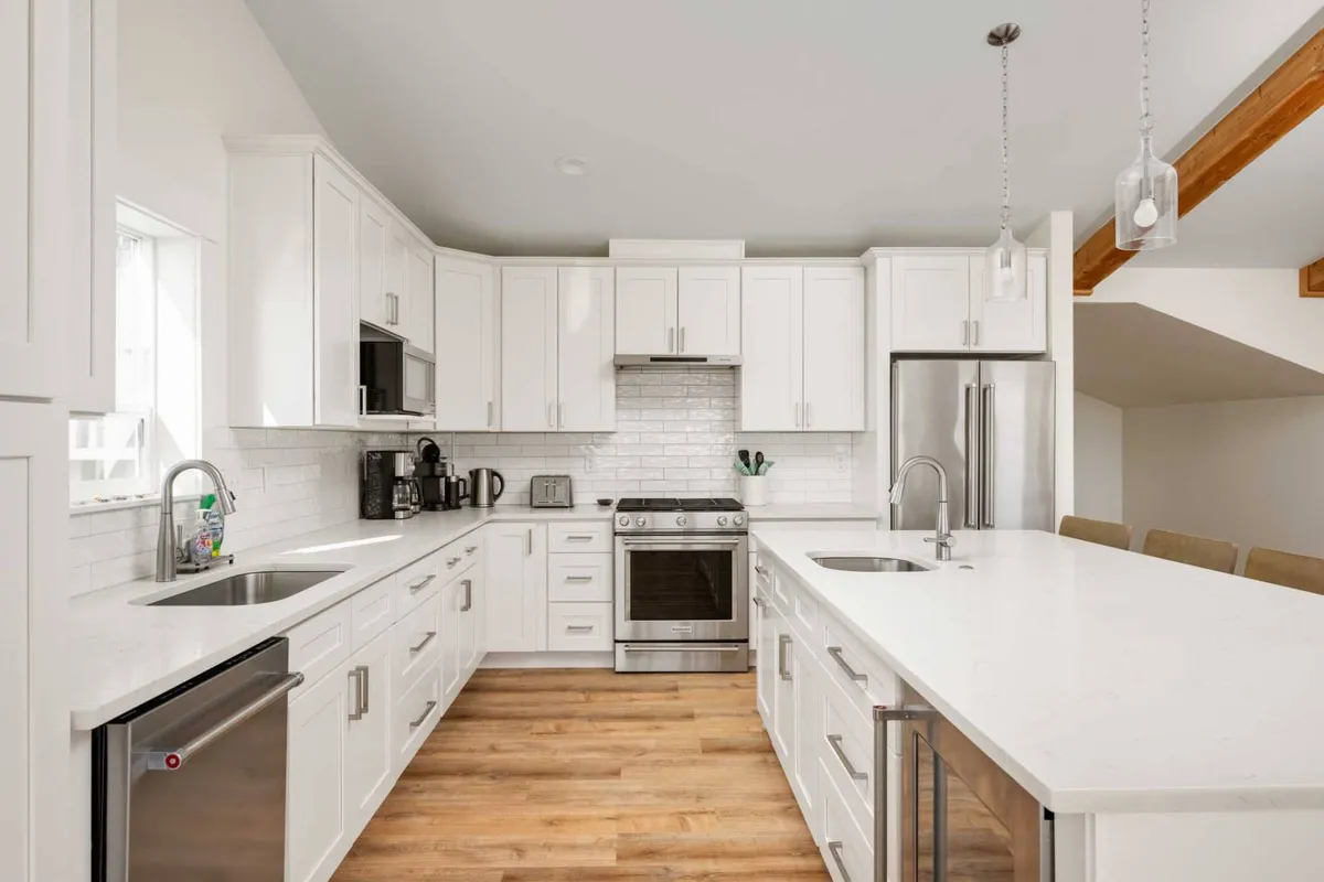A modern kitchen with a central island, stainless steel appliances, white cabinetry, and natural wood accents. The room is designed for cooking, entertaining, and family gatherings.