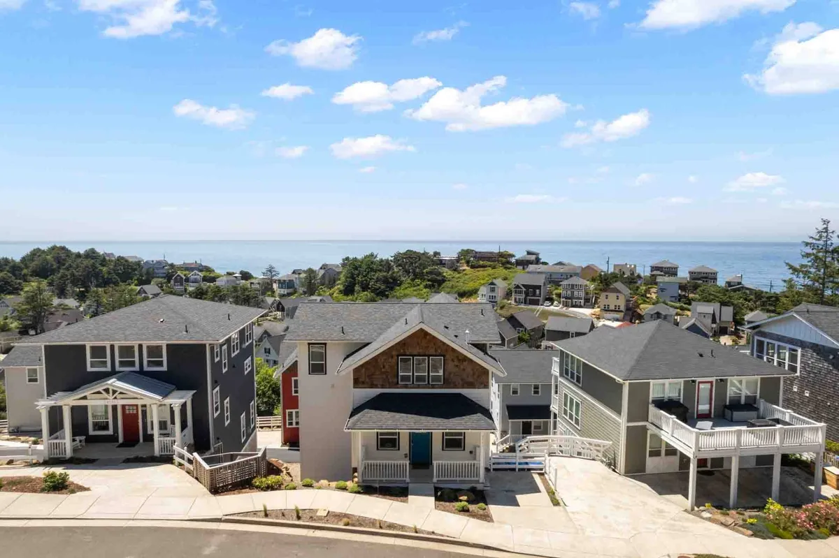 A vibrant exterior shot showcasing colorful houses in the Olivia Beach community with beautifully landscaped gardens and a partial view of the ocean beyond. The scene exudes a cheerful, family-friendly vibe and suggests easy access to both the beach and shared outdoor spaces.
