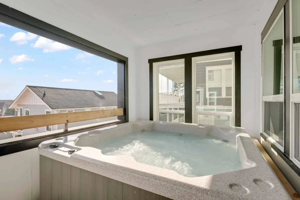 A serene indoor hot tub area with large windows framing views of the outdoors. The hot tub is spacious, inviting, and positioned to take in sunset views, blending relaxation with scenic beauty.