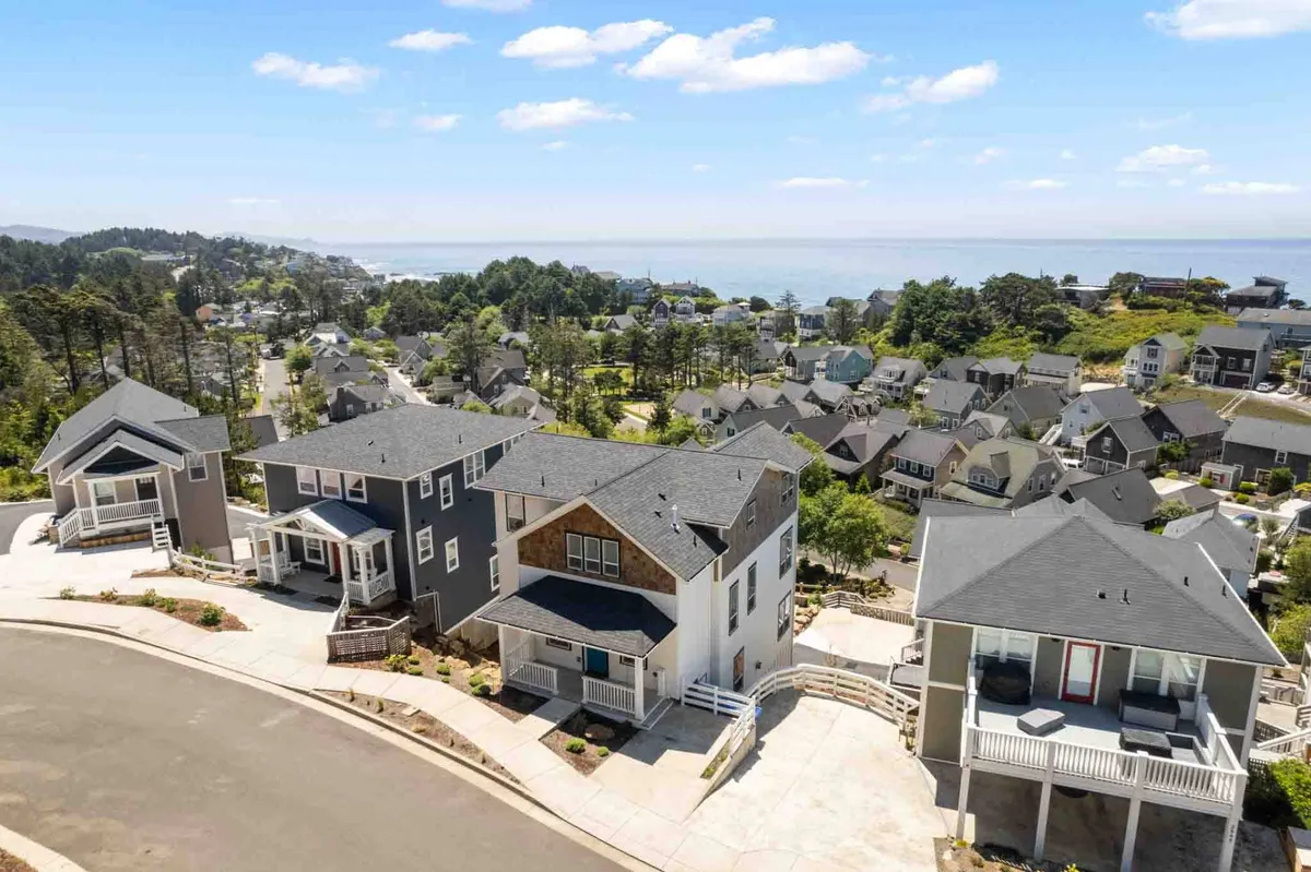A panoramic view showcasing the neighborhood’s modern architecture nestled along the coastline, with porches looking out toward the ocean. The scene conveys a serene, picturesque environment ideal for both coastal walks and exploring the vibrant local community.