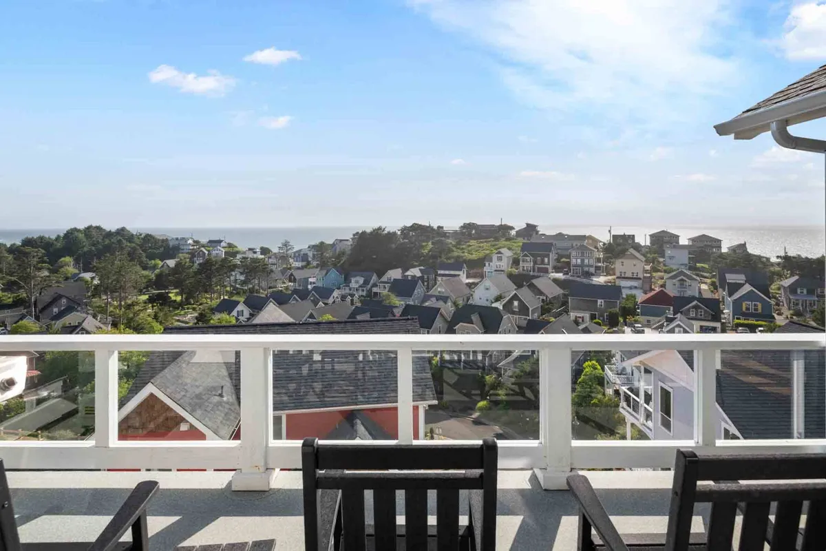 A balcony scene featuring outdoor seating, ocean views, and a glimpse of a picturesque neighborhood. The tranquil setting is ideal for morning coffee, relaxing, or enjoying the sunset.