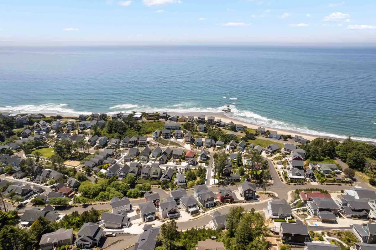 An elevated, tranquil view over the neighborhood with the ocean visible in the distance, surrounded by trees and houses. The scene hints at the easy transition from home to beach and the natural beauty that surrounds the area.