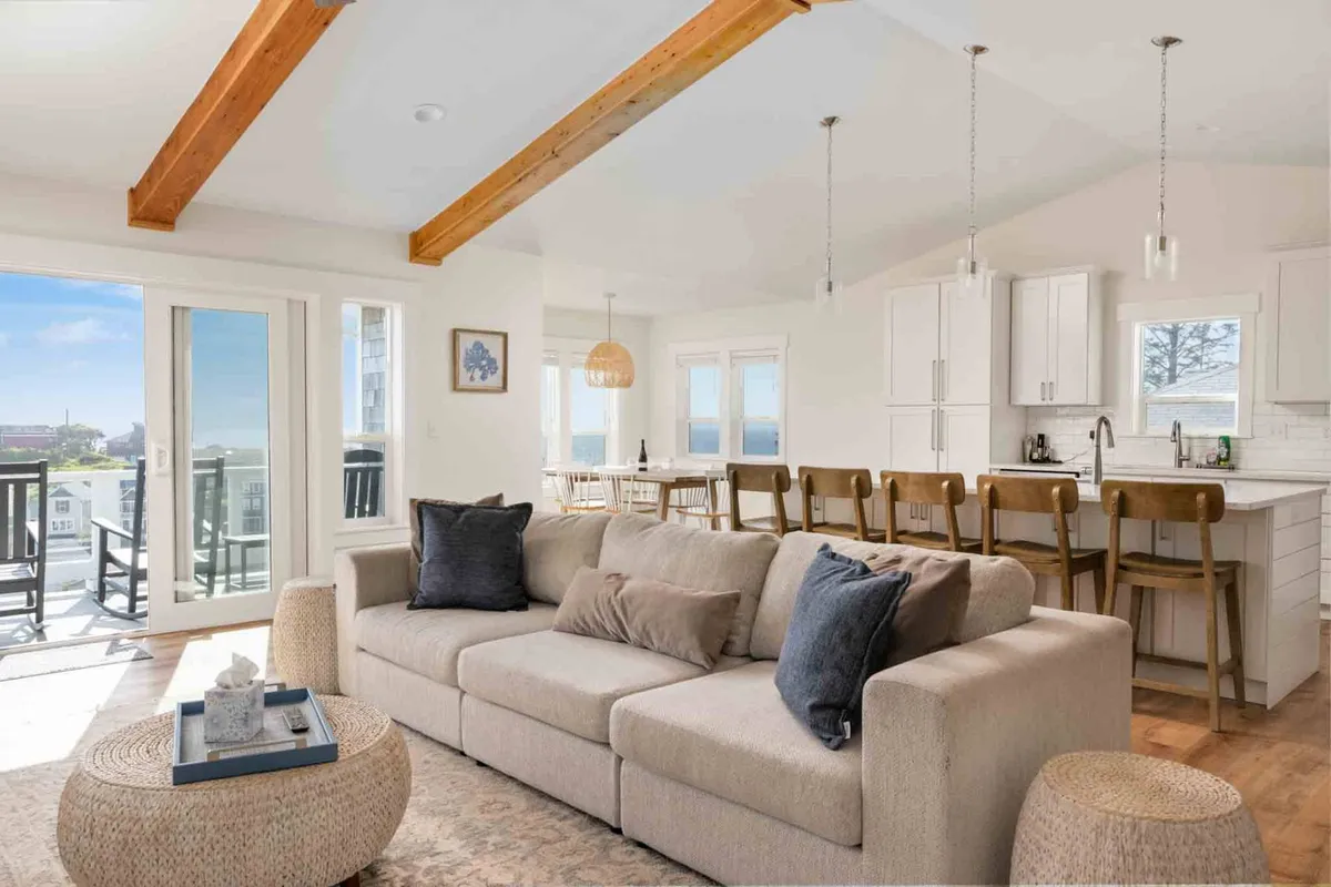 A spacious open-concept room featuring a cozy sofa, a central kitchen island, a stylish dining area, and large windows that flood the space with natural light. The inviting atmosphere is enhanced by coordinated décor that connects the living, dining, and kitchen spaces seamlessly.