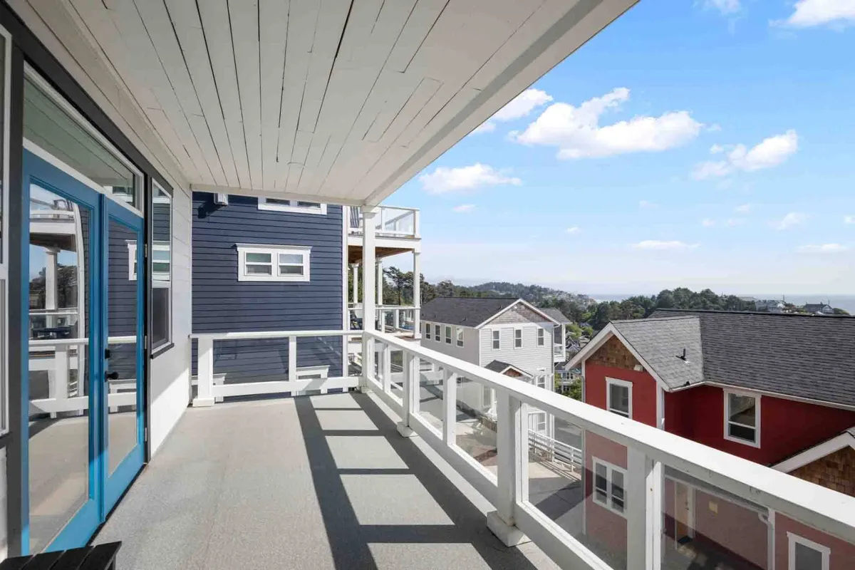 This image features a welcoming exterior scene with a bright blue door, a view of the surrounding landscape, and colorful neighboring houses. The inviting space suggests a connection to the outside world and a sense of community, ideal for gatherings and outdoor relaxation.